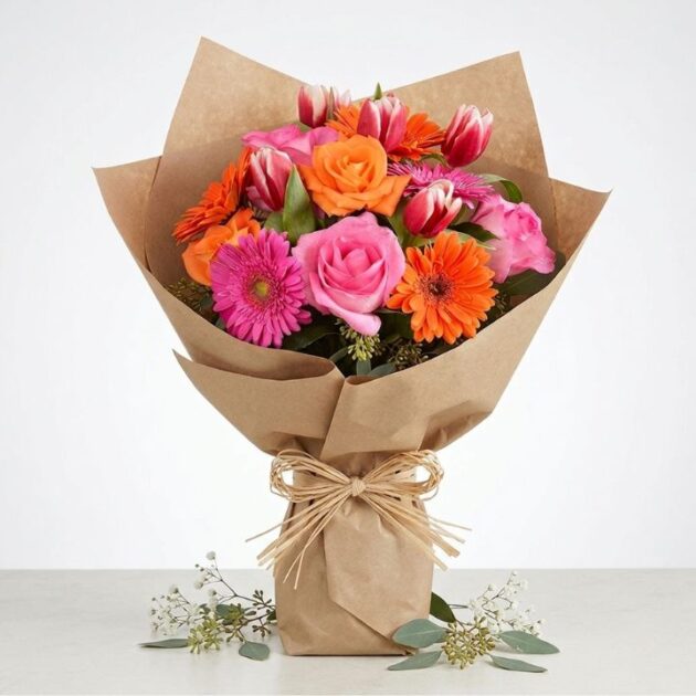 A vibrant tulip and gerbera daisy bouquet arranged with fresh greenery in a clean studio setting.